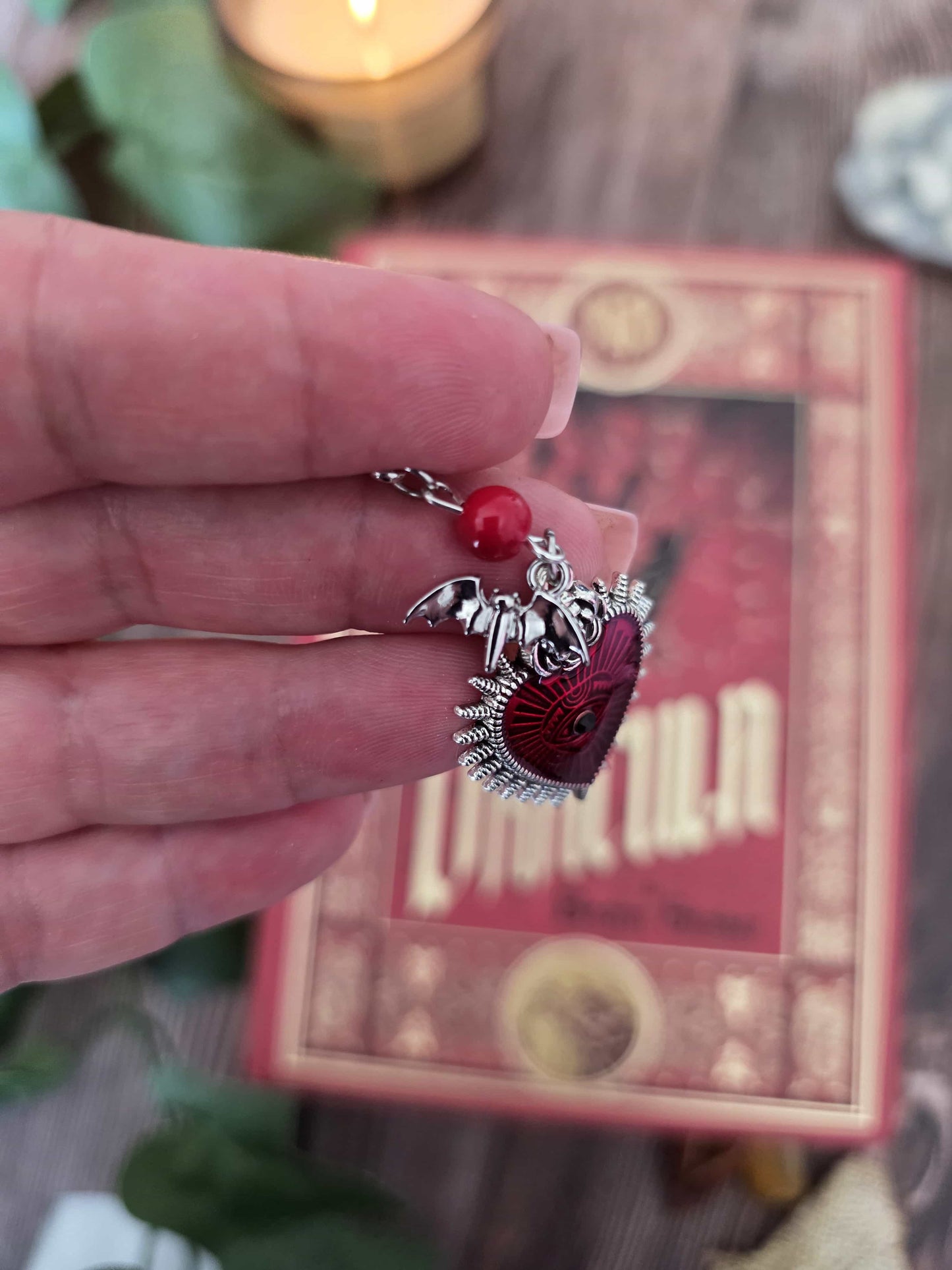 Marque-page en métal vampire, chauve-souris avec un gros coeur rouge. Parfait pour les lecteur.ices de livres fantastiques, fantasy et gothique. Pierres naturelles personnalisables. Corail rouge. Bellette Workshop. zoom sur la breloque chauve-souris