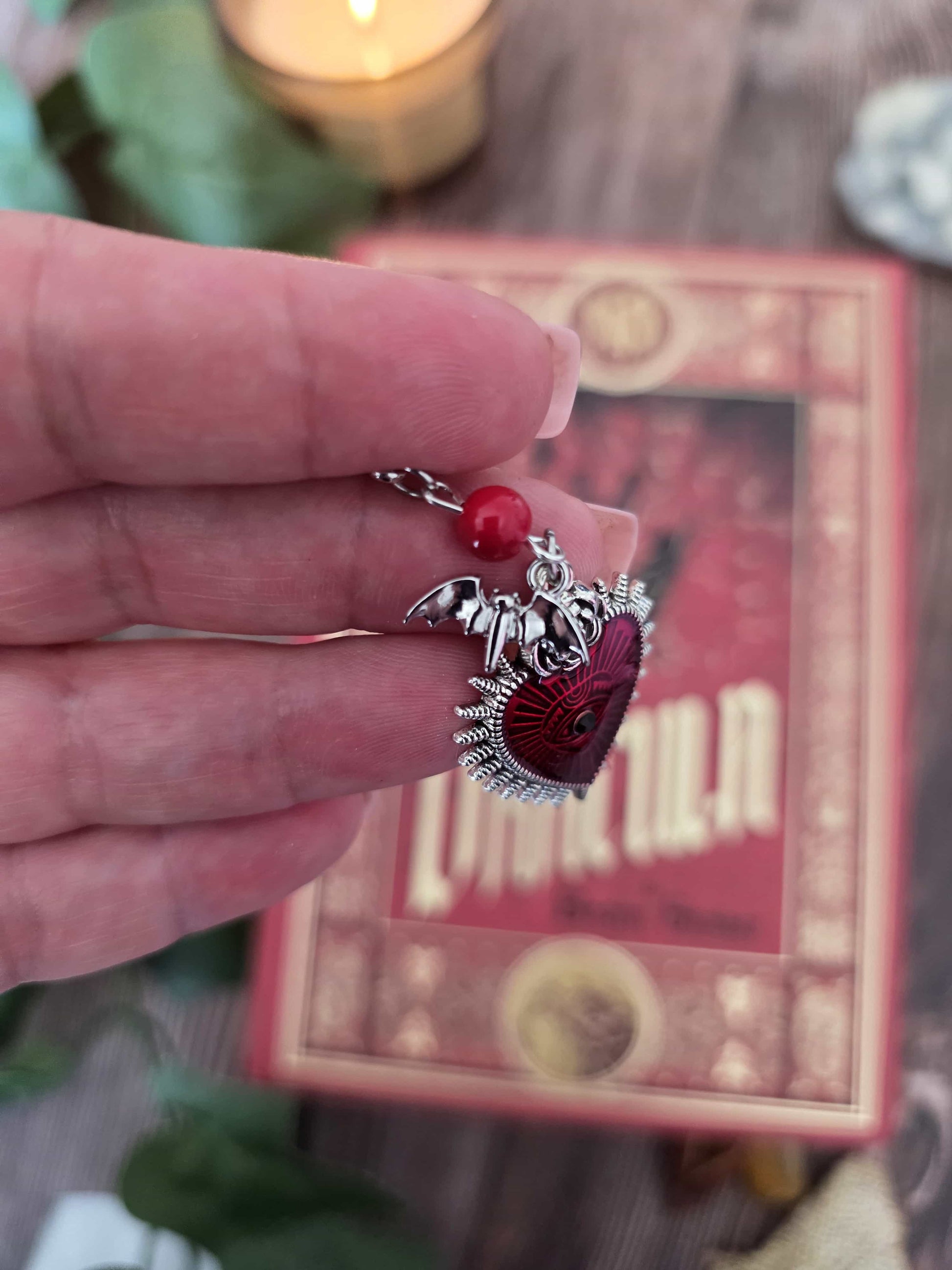Marque-page en métal vampire, chauve-souris avec un gros coeur rouge. Parfait pour les lecteur.ices de livres fantastiques, fantasy et gothique. Pierres naturelles personnalisables. Corail rouge. Bellette Workshop. zoom sur la breloque chauve-souris