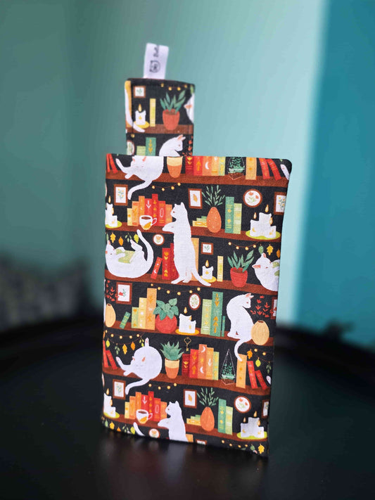 Couvre-livre artisanal ajustable aux nombres de pages et à l'épaisseur du livre. Motif tissu en coton chat bibliothèque avec son marque-page en tissu assorti. Posé sur une table noire.