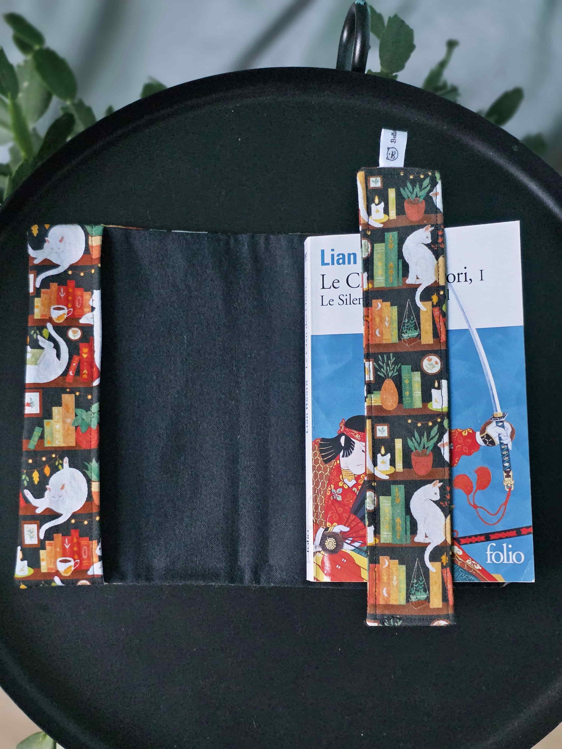 Couvre-livre artisanal ajustable aux nombres de pages et à l'épaisseur du livre. Motif tissu en coton chat bibliothèque avec son marque-page en tissu assorti. Ouvert sur la flanelle noire en coton toute douce