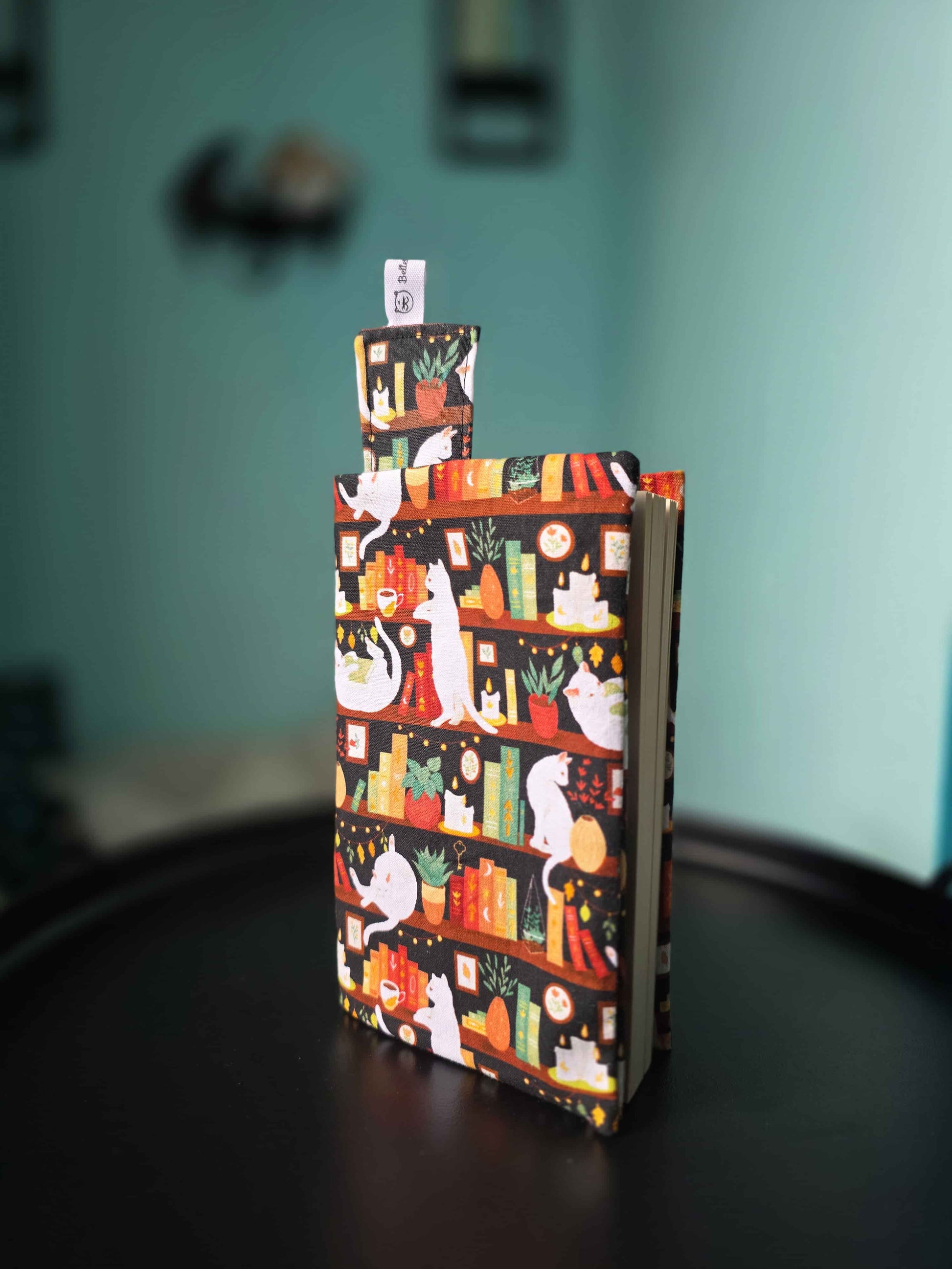 Couvre-livre artisanal ajustable aux nombres de pages et à l'épaisseur du livre. Motif tissu en coton chat bibliothèque avec son marque-page en tissu assorti. vu de profil