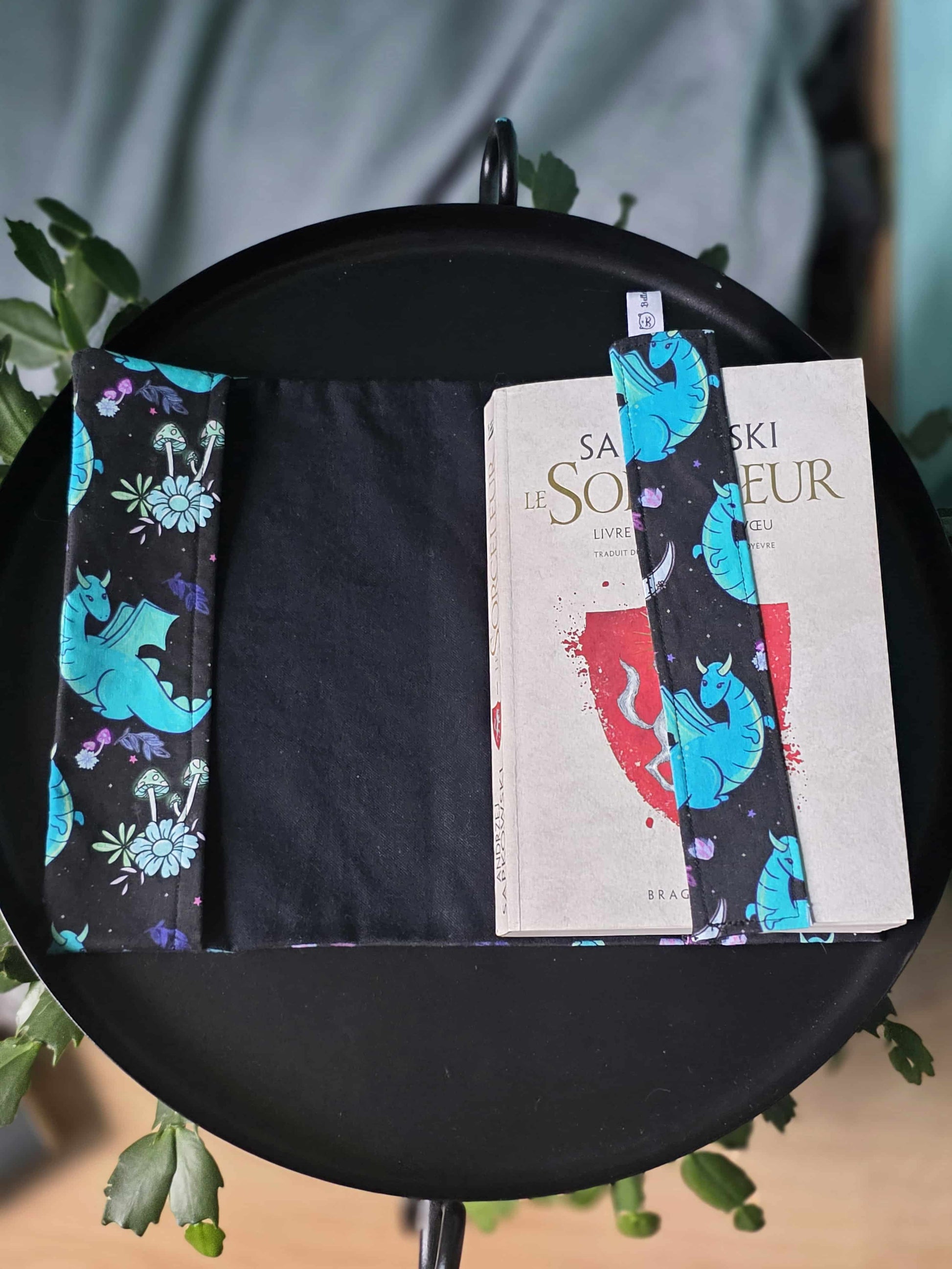 Couvre-livre artisanal et ajustable ouvert avec le marque-page en tissu assorti en tissu thermocollé. Motif dragon et fantasy