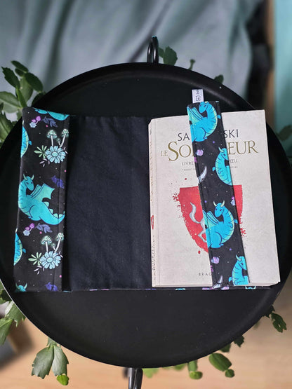 Couvre-livre artisanal et ajustable ouvert avec le marque-page en tissu assorti en tissu thermocollé. Motif dragon et fantasy
