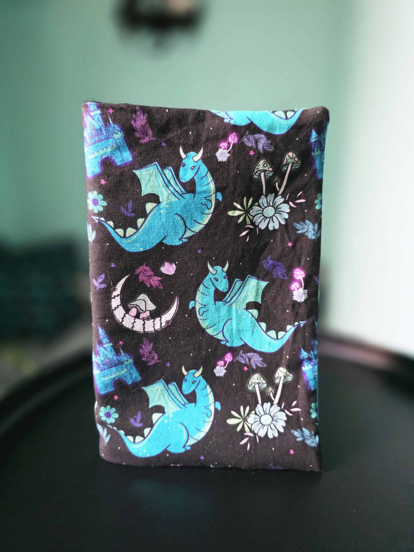 couvre-livre artisanal en coton motif fantasy bleu et violet, dragon, fait main, posé debout sur une table noire 