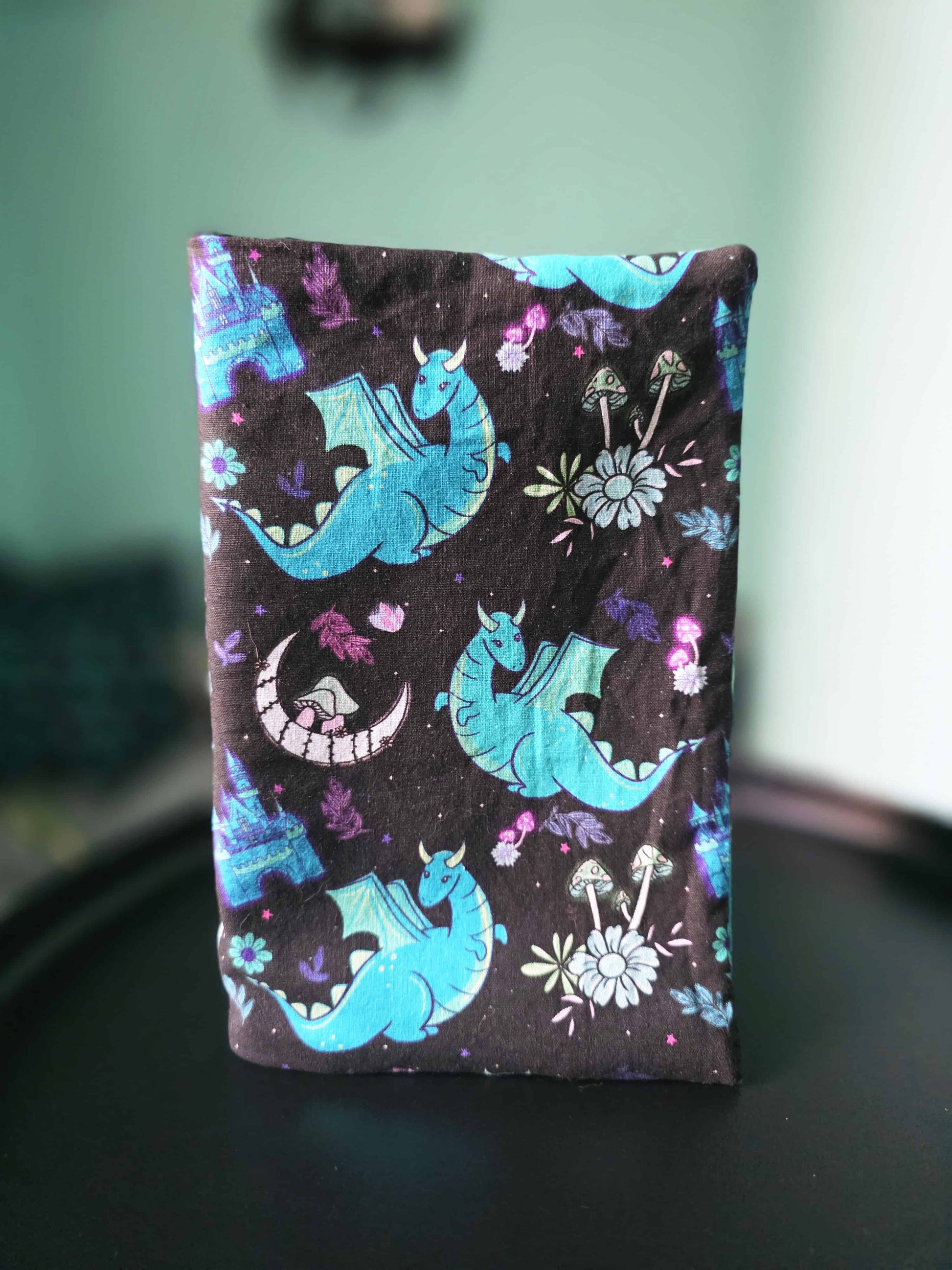 couvre-livre artisanal en coton motif fantasy bleu et violet, dragon, fait main, posé debout sur une table noire 