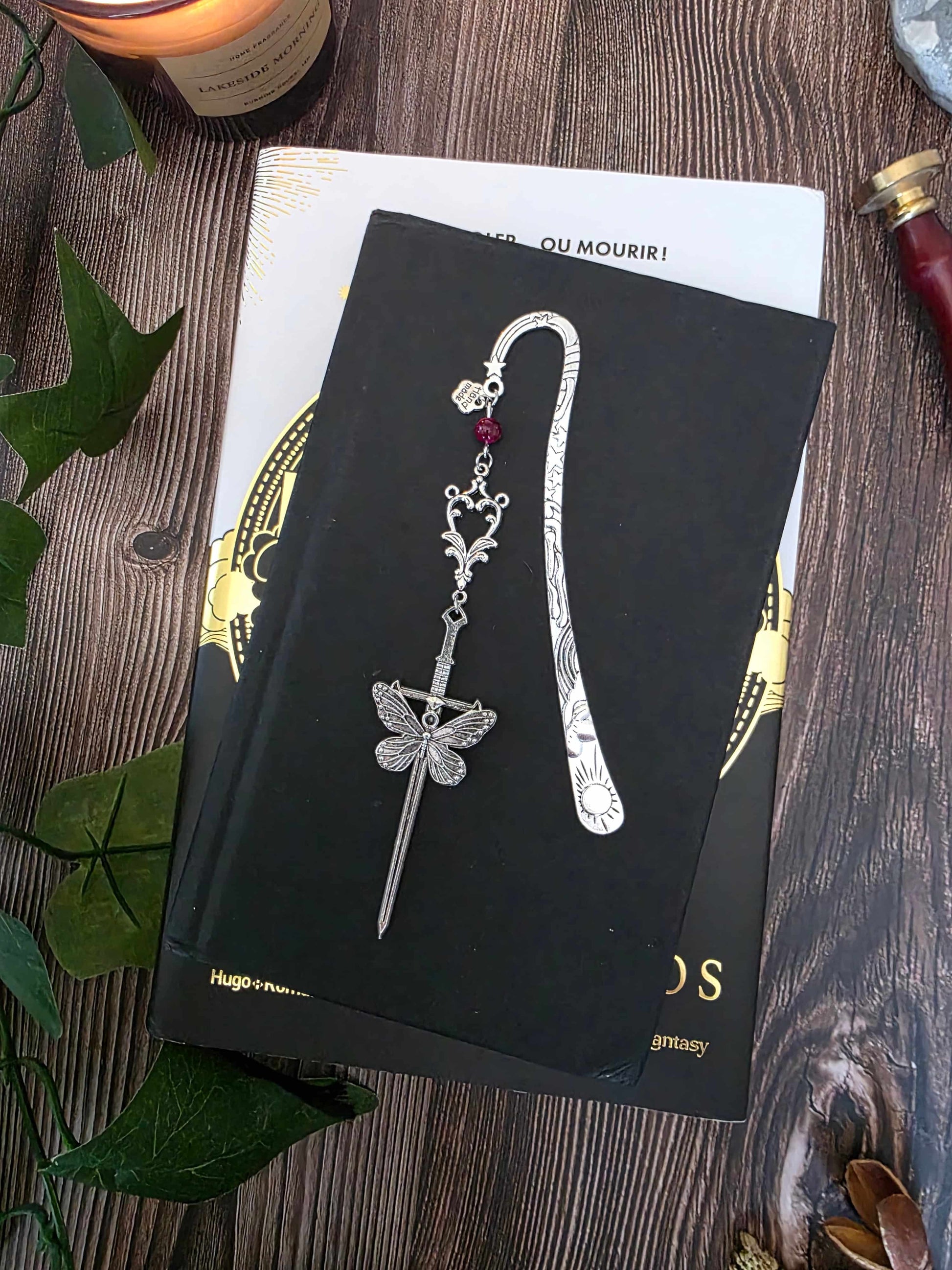 marque-page en métal d'une épée avec un gros papillon. Entrelacs. Inspirée par la fantasy, romantasy, dark fantasy. Fait main par belletteworkshop. pierre naturelle d'oeil de tigre rose, personnalisable. le bijou de livre est posé sur le livre fourth wing