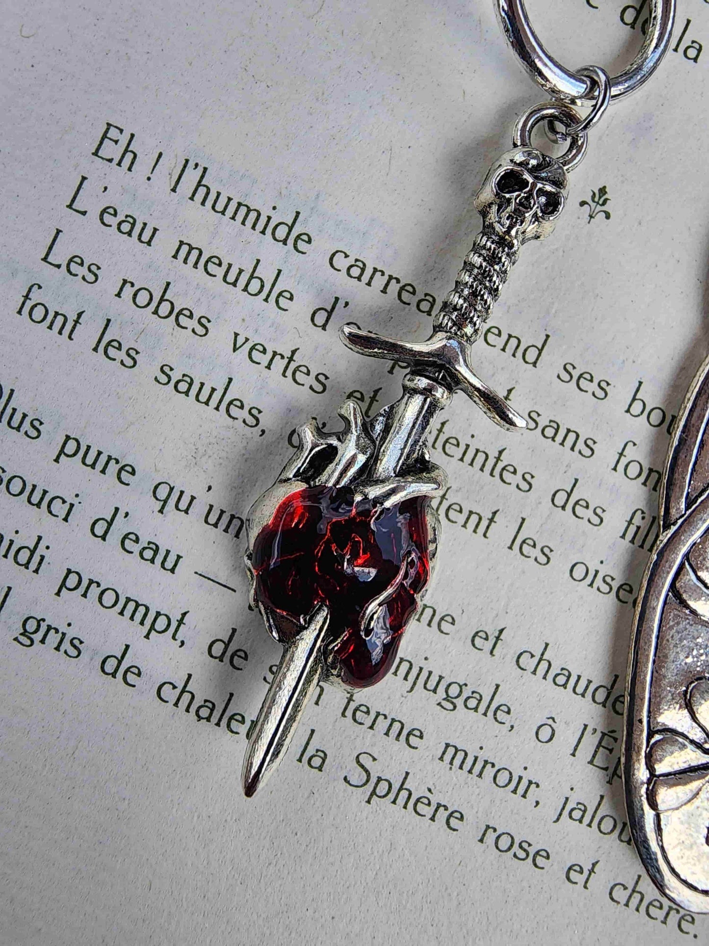 Zoom sur le détail des breloques du marque-page romantasy : épée qui transperce un cœur humain rouge.
