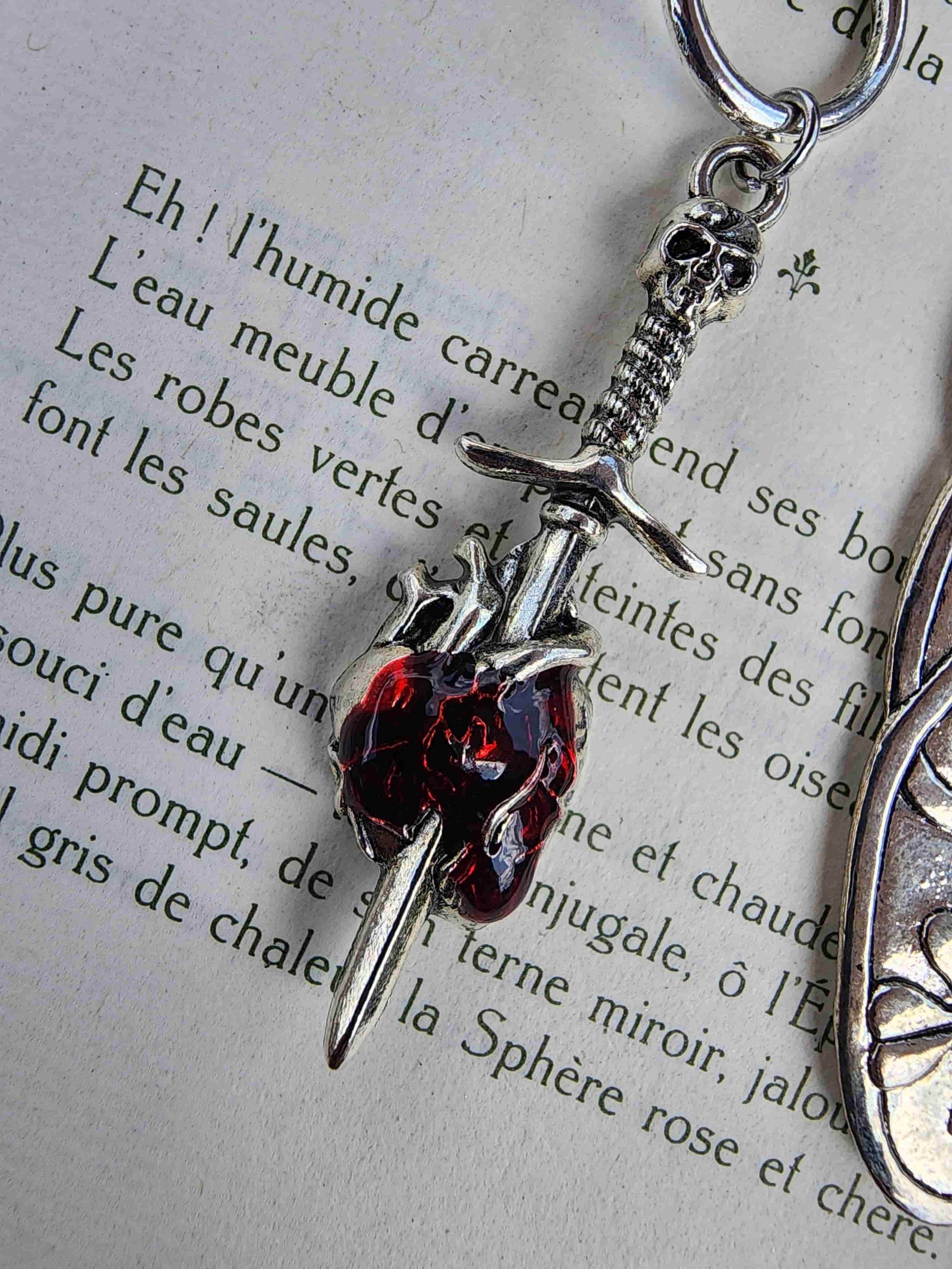 Zoom sur le détail des breloques du marque-page romantasy : épée qui transperce un cœur humain rouge.