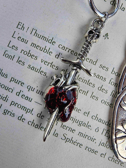Zoom sur le détail des breloques du marque-page romantasy : épée qui transperce un cœur humain rouge.