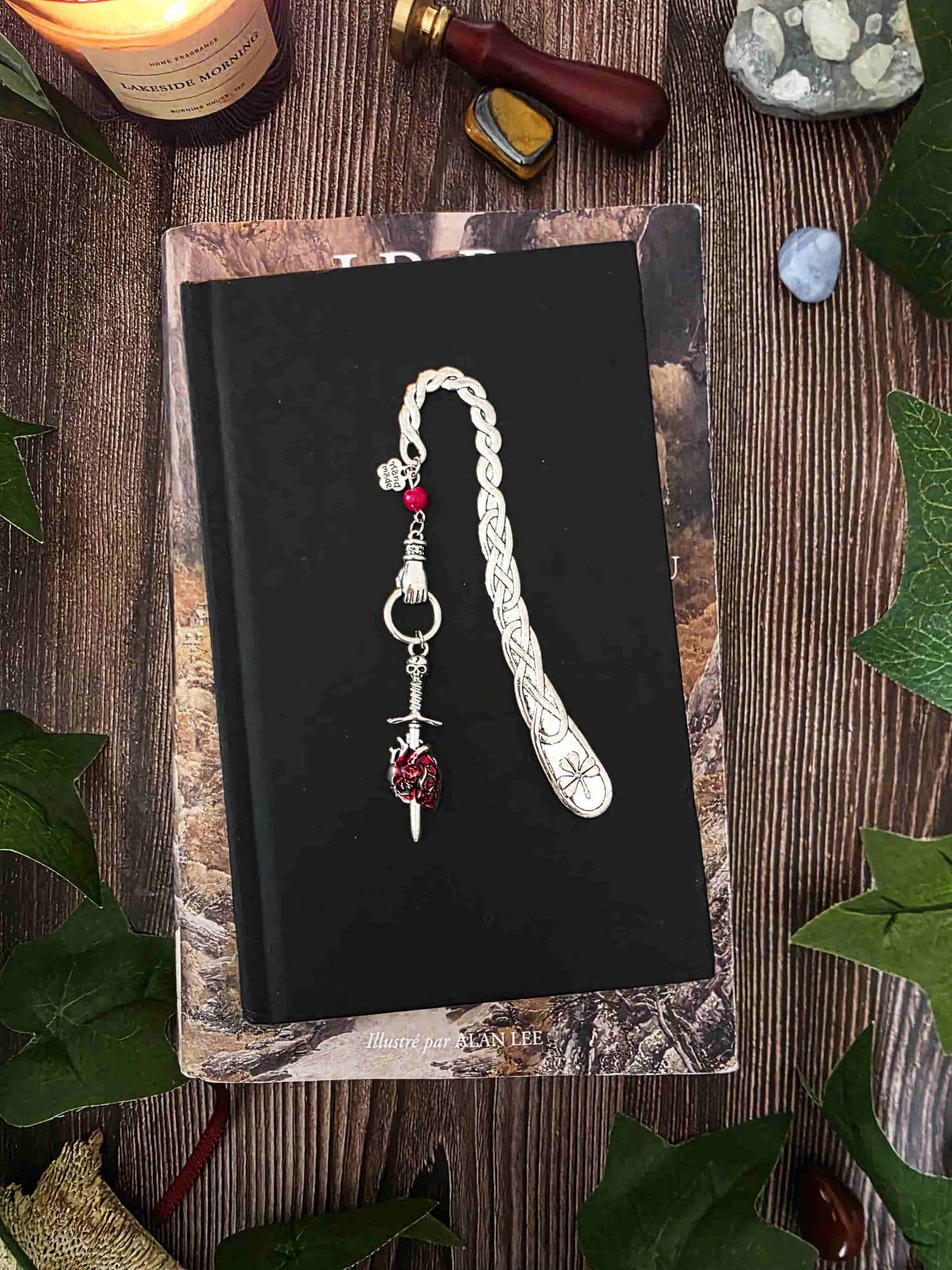Marque-page "Le voeu de l'épée", un coeur humain transpercé par une épée, avec une breloque main au dessus qui tient l'épée ainsi qu'une pierre naturelle de corail rouge. Le signet est en métal et évoque un bijou de livre très beau pour les romans de fantasy, dark fantasy et romantasy