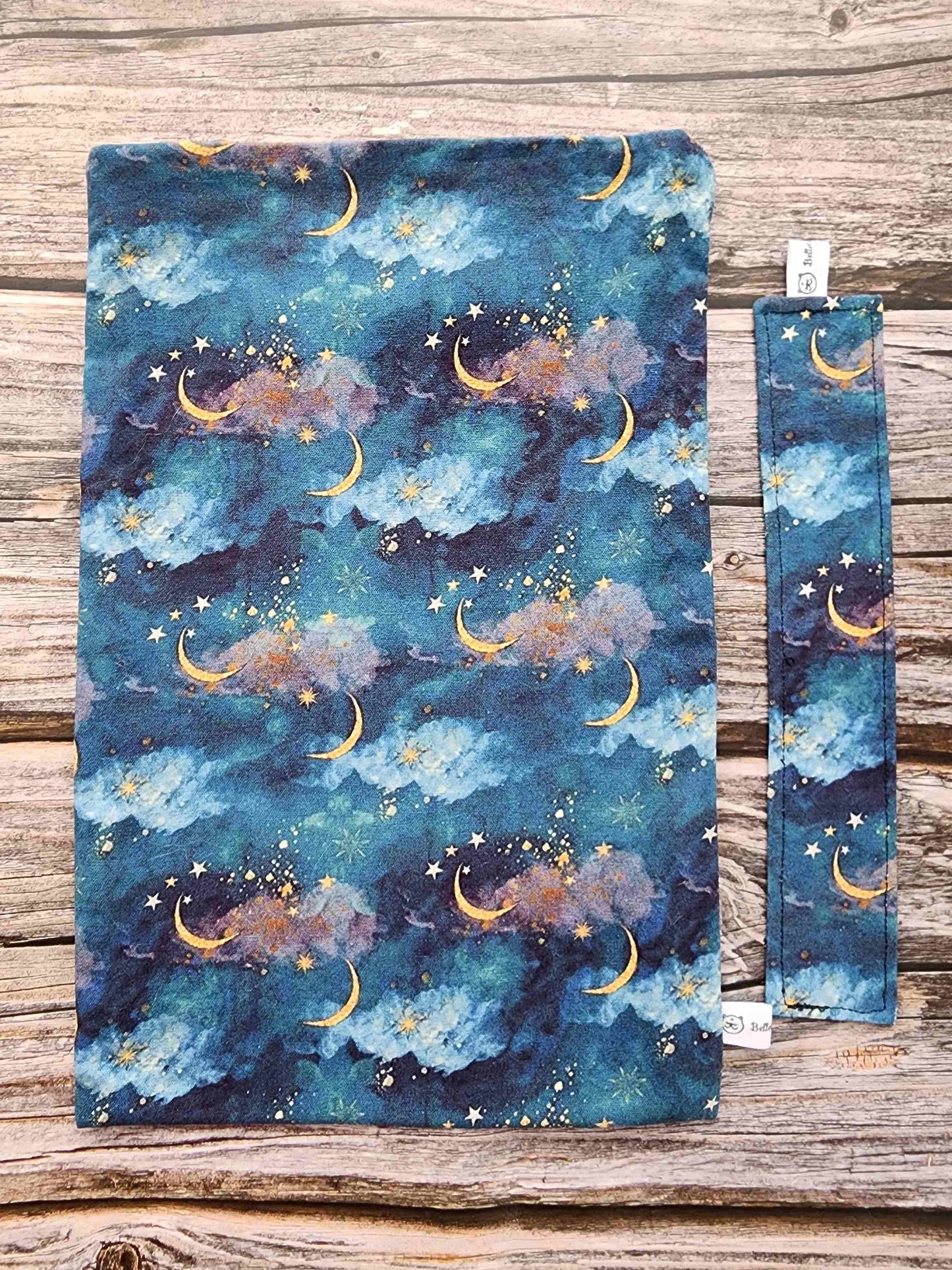 pochettte à livre, booksleeve, en tissu avec un joli ciel étoilé avec des lunes dorées. Fait main en Bretagne par Bellette Workshop. Avec un marque-page en tissu assorti en option possible.