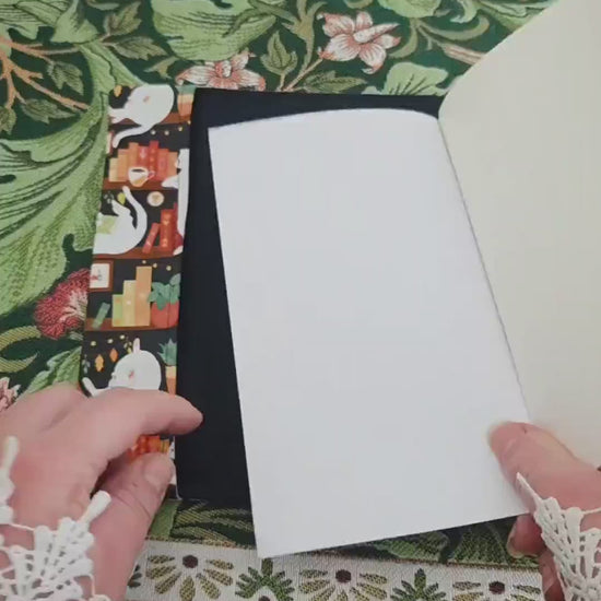 Vidéo de 10 secondes qui montre le couvre-livre artisanal ajustable aux nombres de pages et à l'épaisseur du livre. Motif tissu en coton chat bibliothèque avec son marque-page en tissu assorti. Bellette Workshop